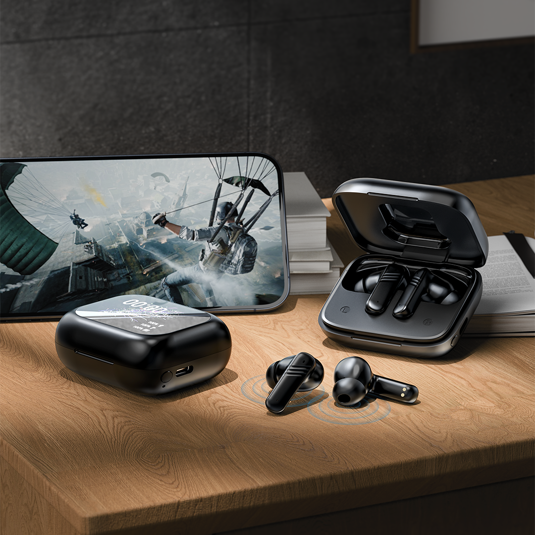 Black wireless earbuds with charging case on a wooden surface, with a smartphone displaying a game in the background.